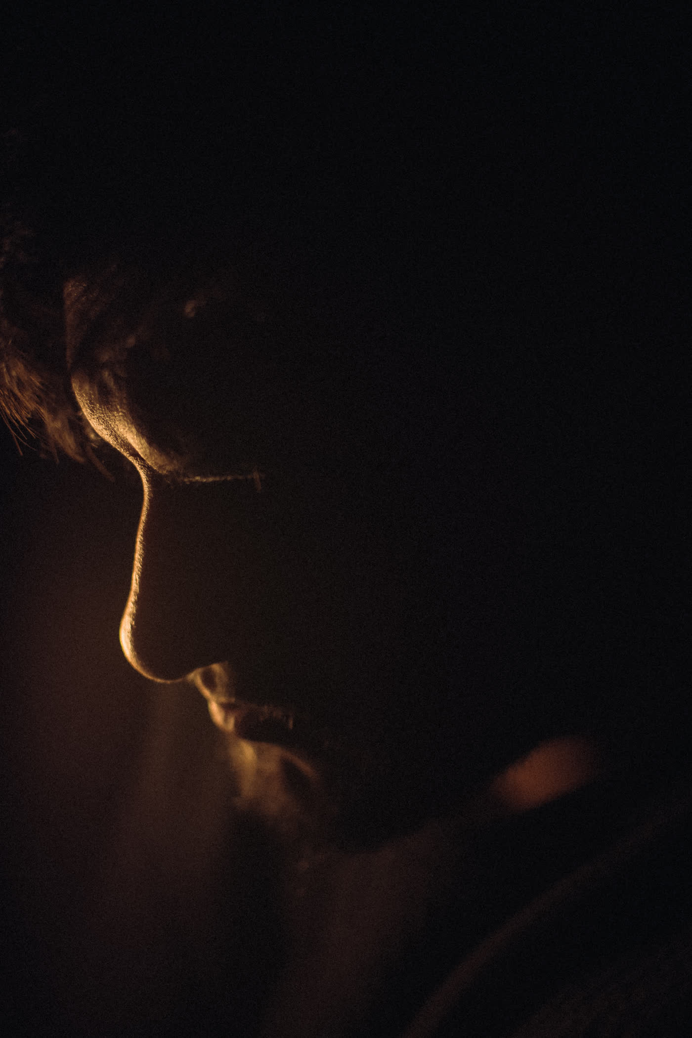 Low-light portrait of a man, face half lit against deep shadow