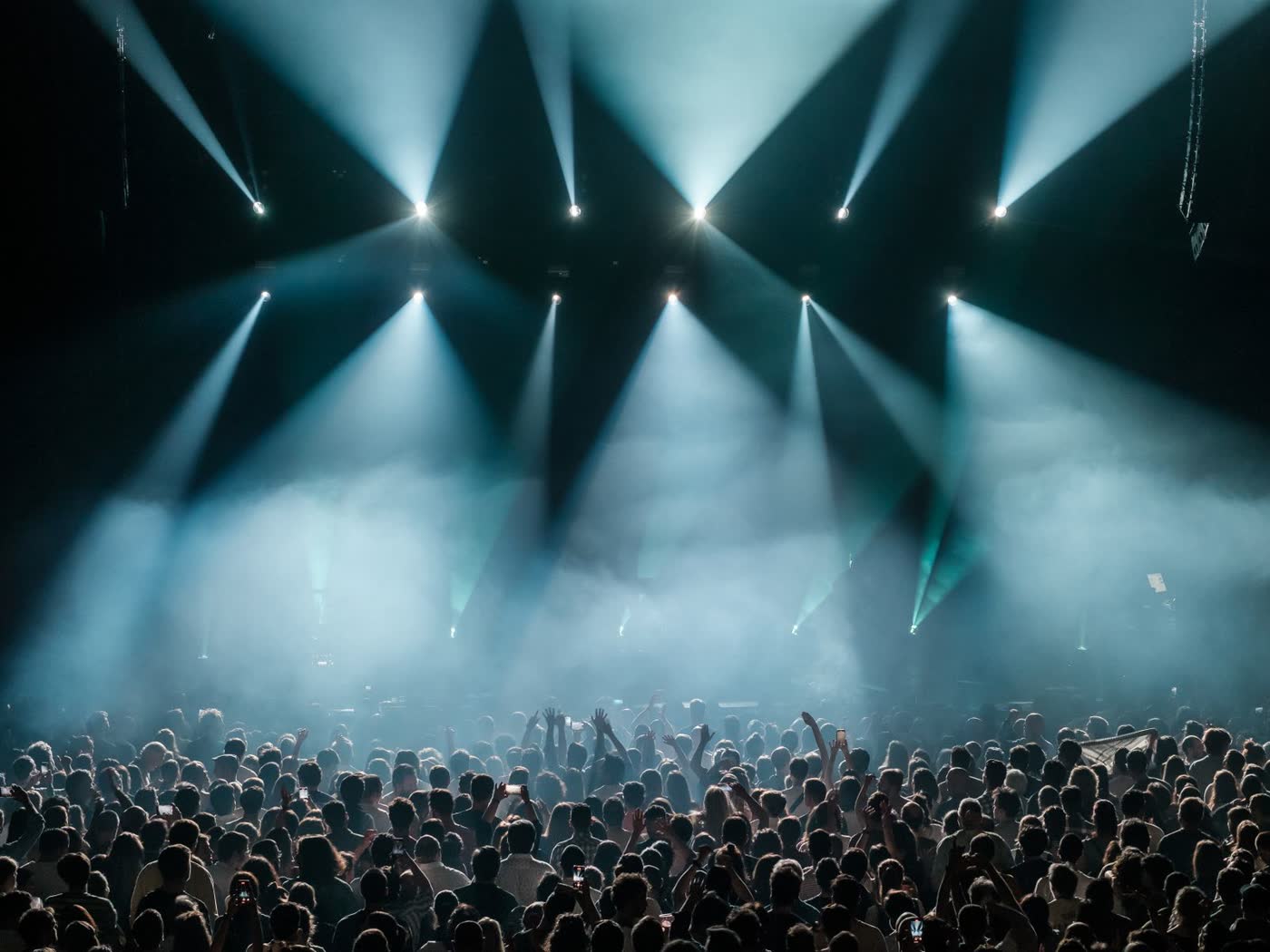 Concert crowd under dramatic stage lighting, hands raised
