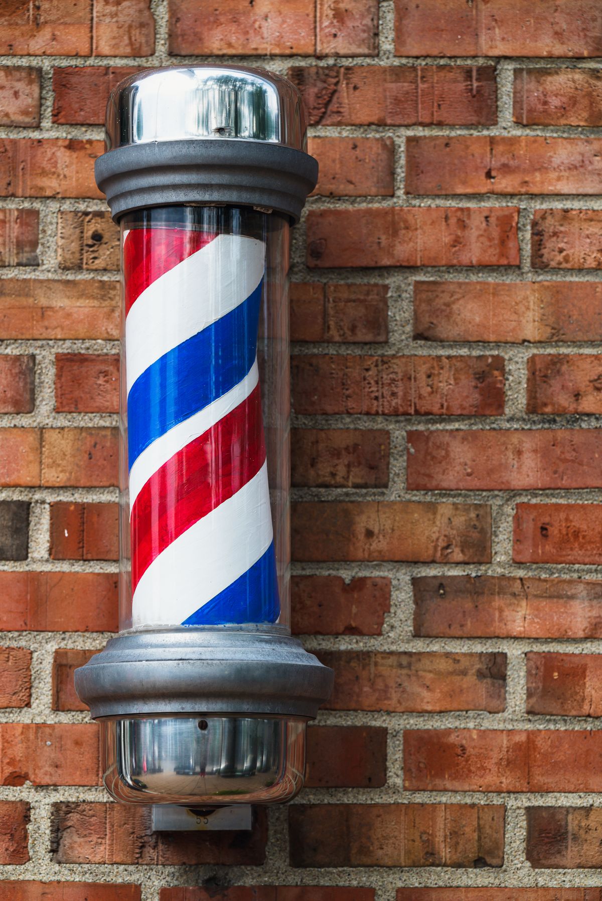 A red, white and blue barber pole mounted on the brick wall outside the shop.